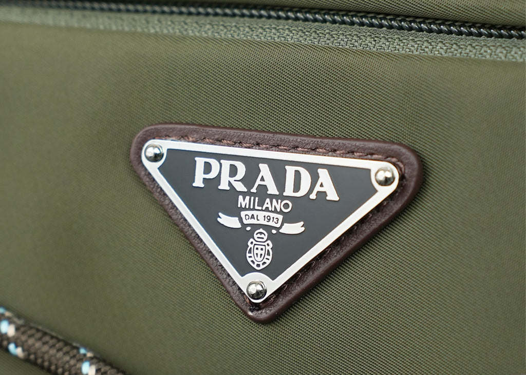 Prada Milano logo patch on green fabric with silver metal border and rivets.