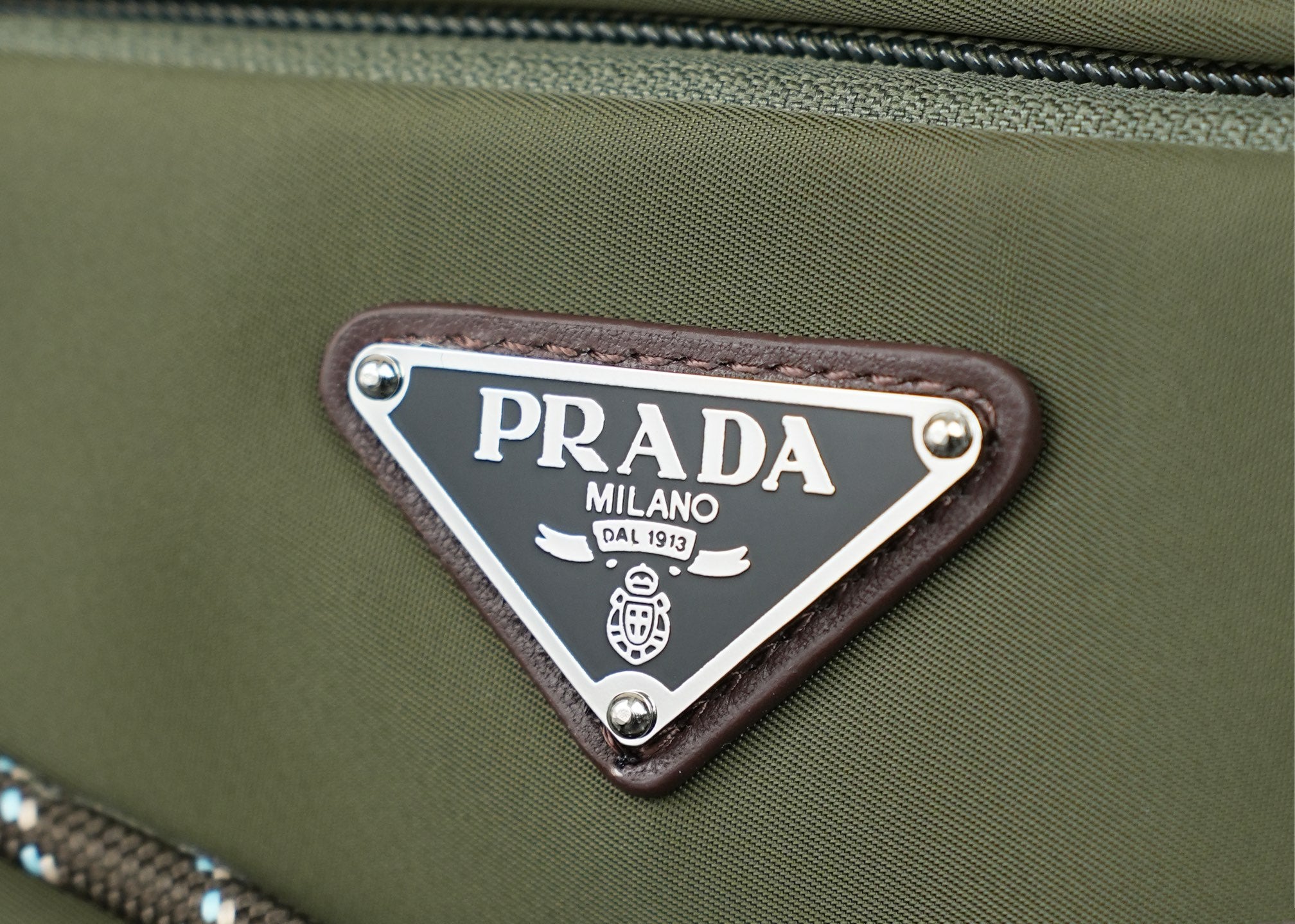 Prada Milano logo patch on green fabric with silver metal border and rivets.