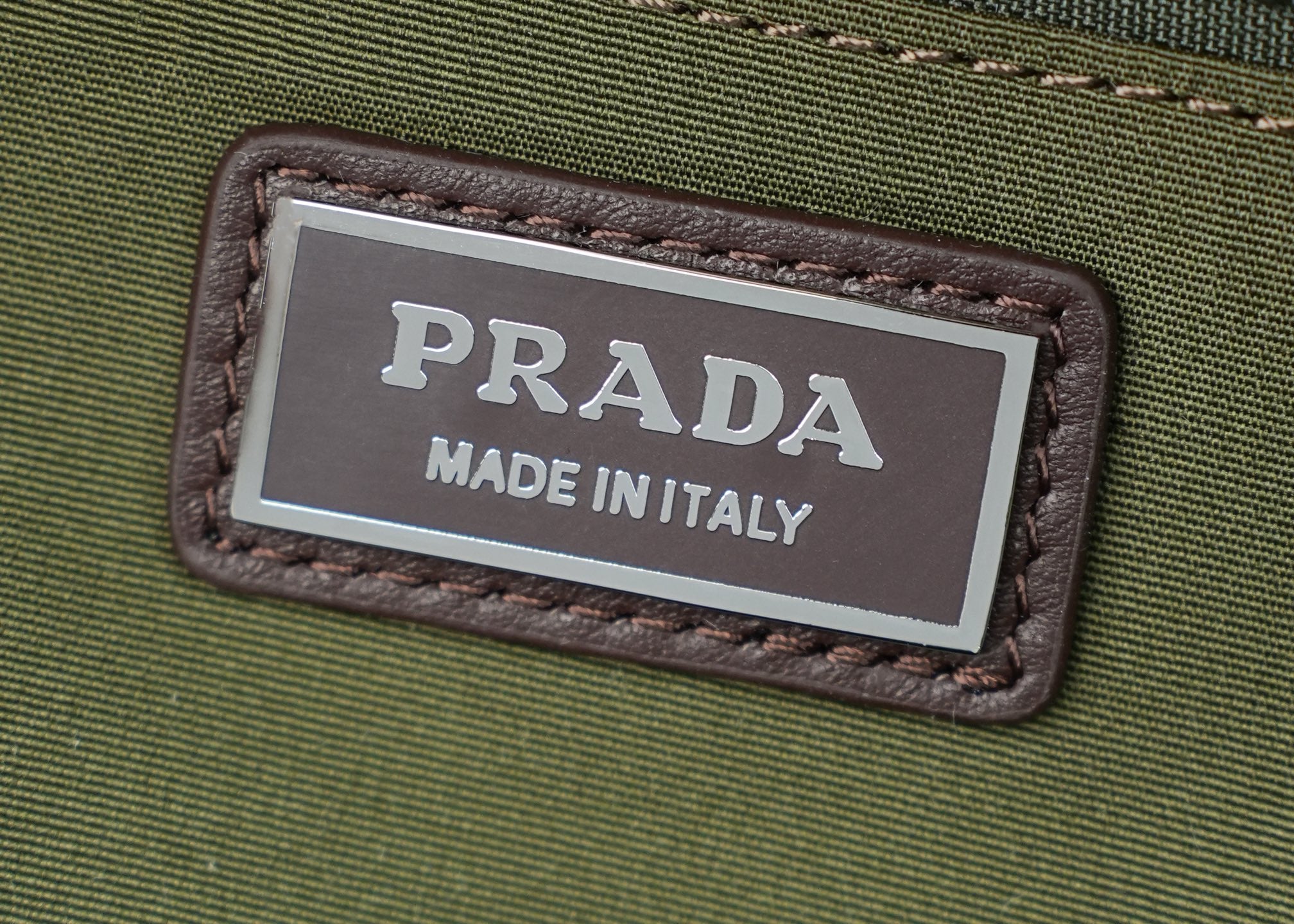 Prada Made in Italy label on green fabric with brown stitched leather border.
