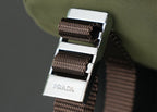 Prada-engraved metal buckle with brown woven webbing strap on green bag.