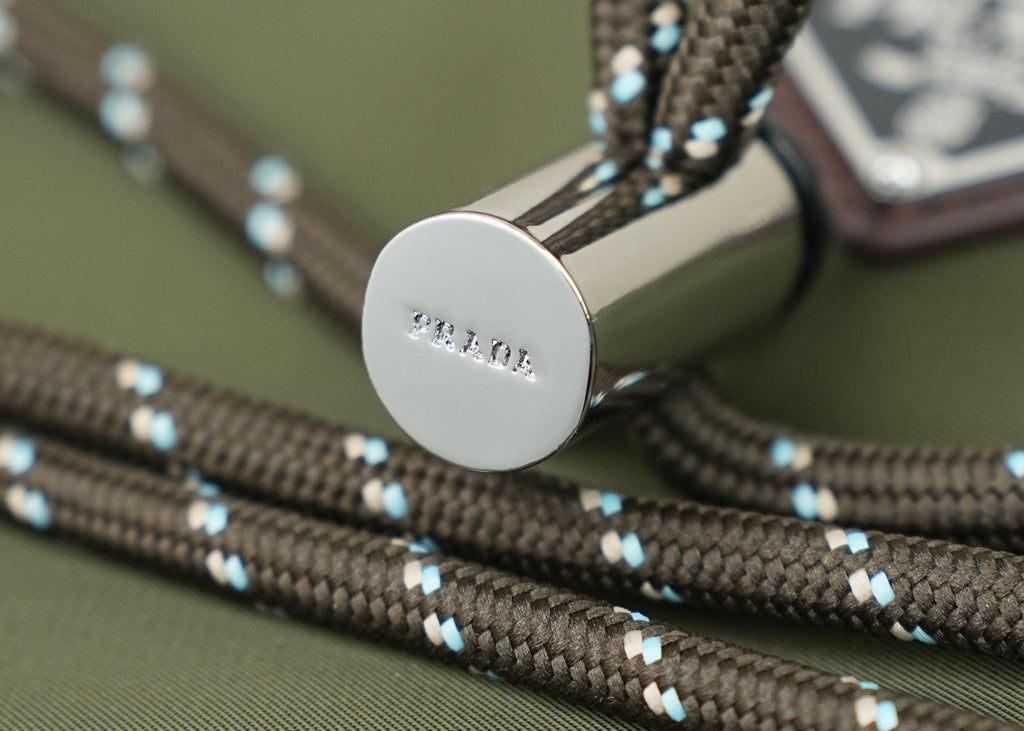Round silver snap button on green bag with blue-and-beige woven trim cords.