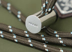 Round silver snap button on green bag with blue-and-beige woven trim cords.