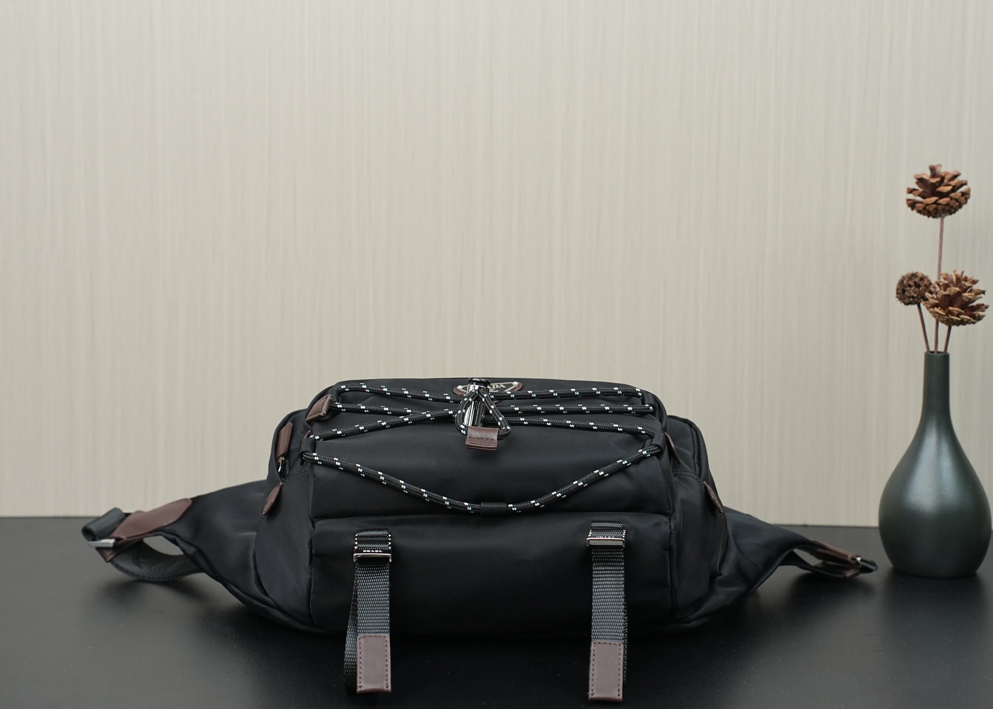 Black belt bag with braided top panel, leather tabs, and front strap loops.