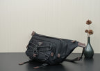Black belt bag with braided trim, front pocket, and brown leather corner tabs.