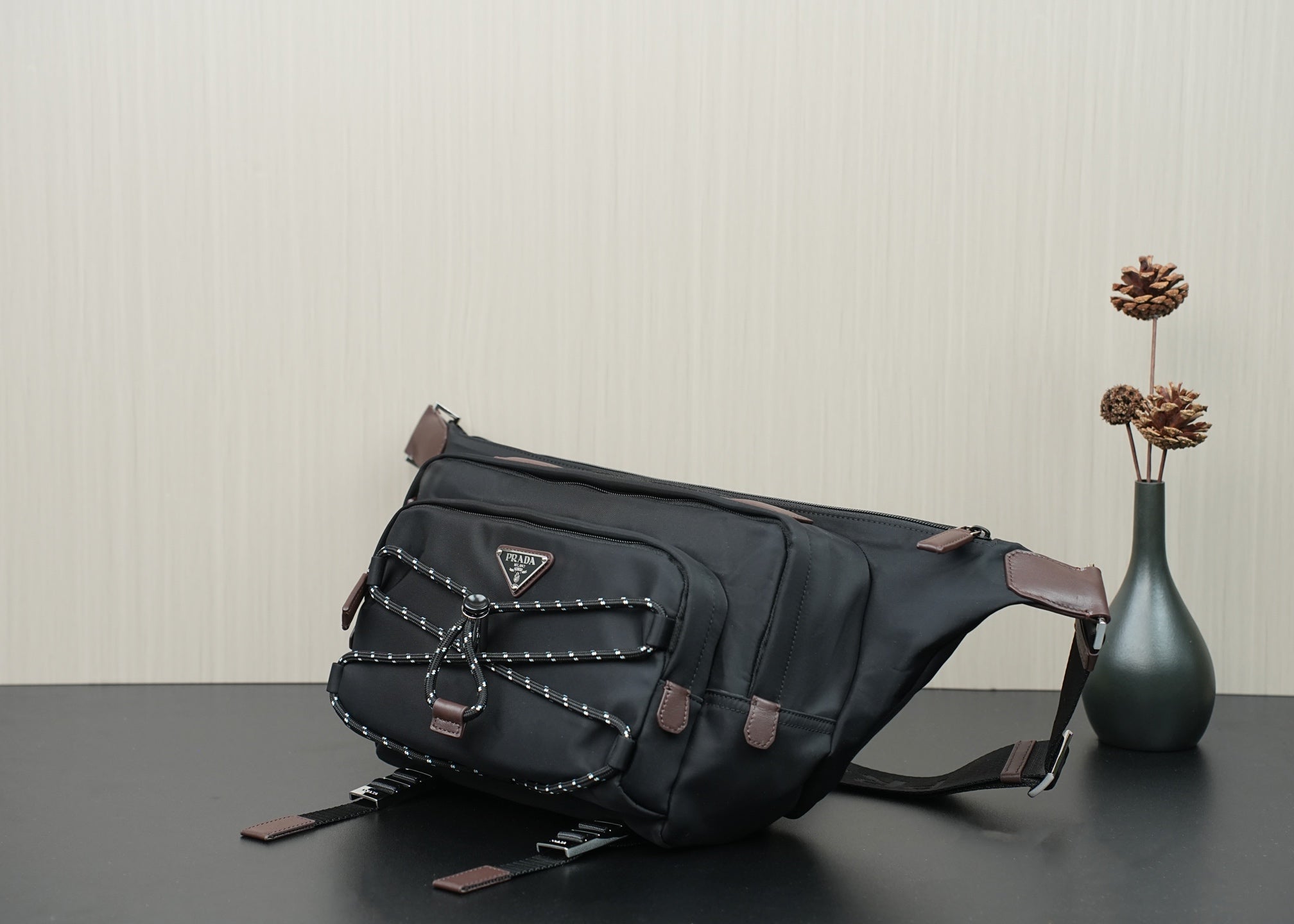 Black belt bag with braided trim, front pocket, and brown leather corner tabs.