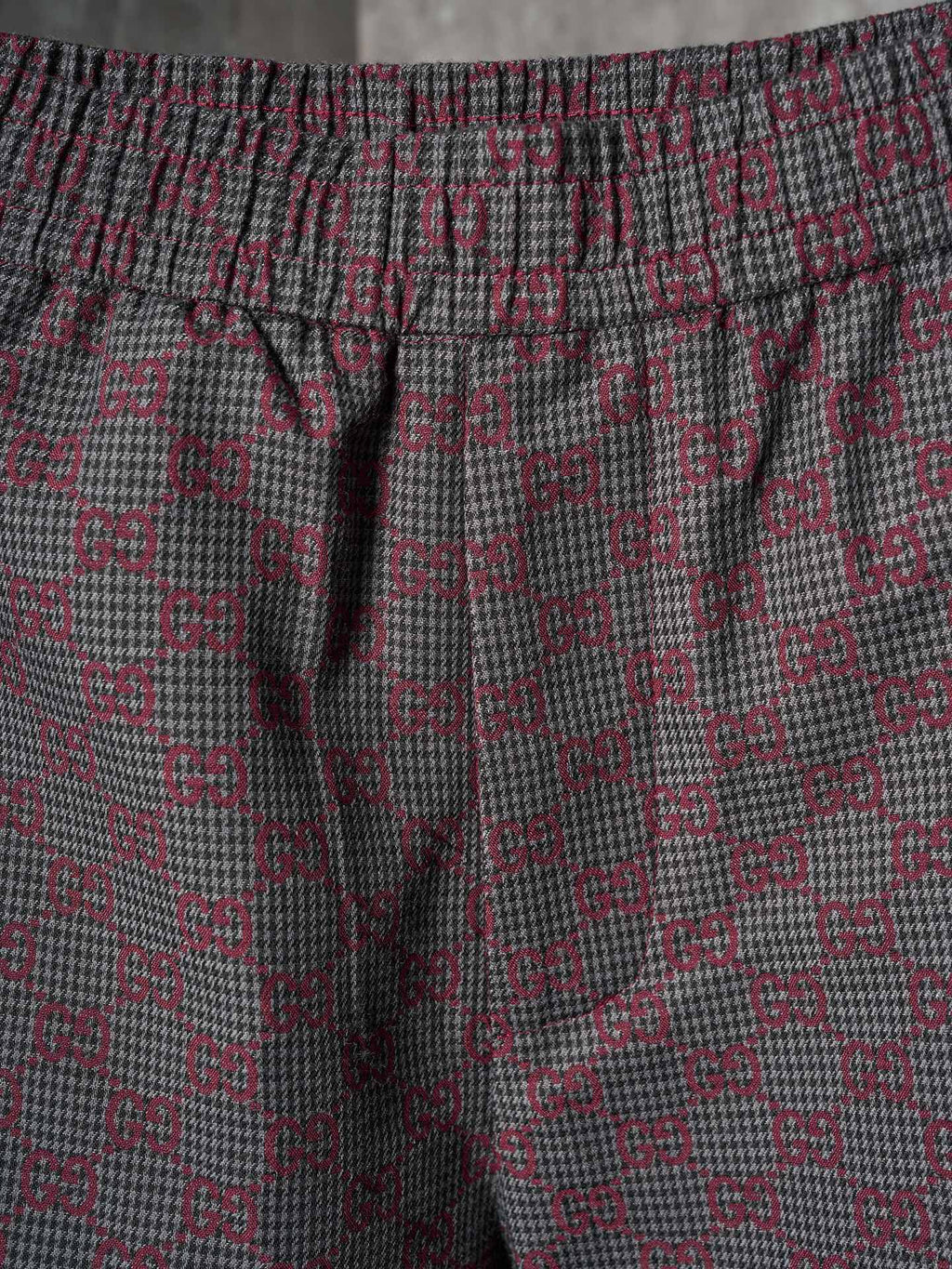 Gucci pants fabric close-up in maroon and gray GG lattice pattern with elastic waistband