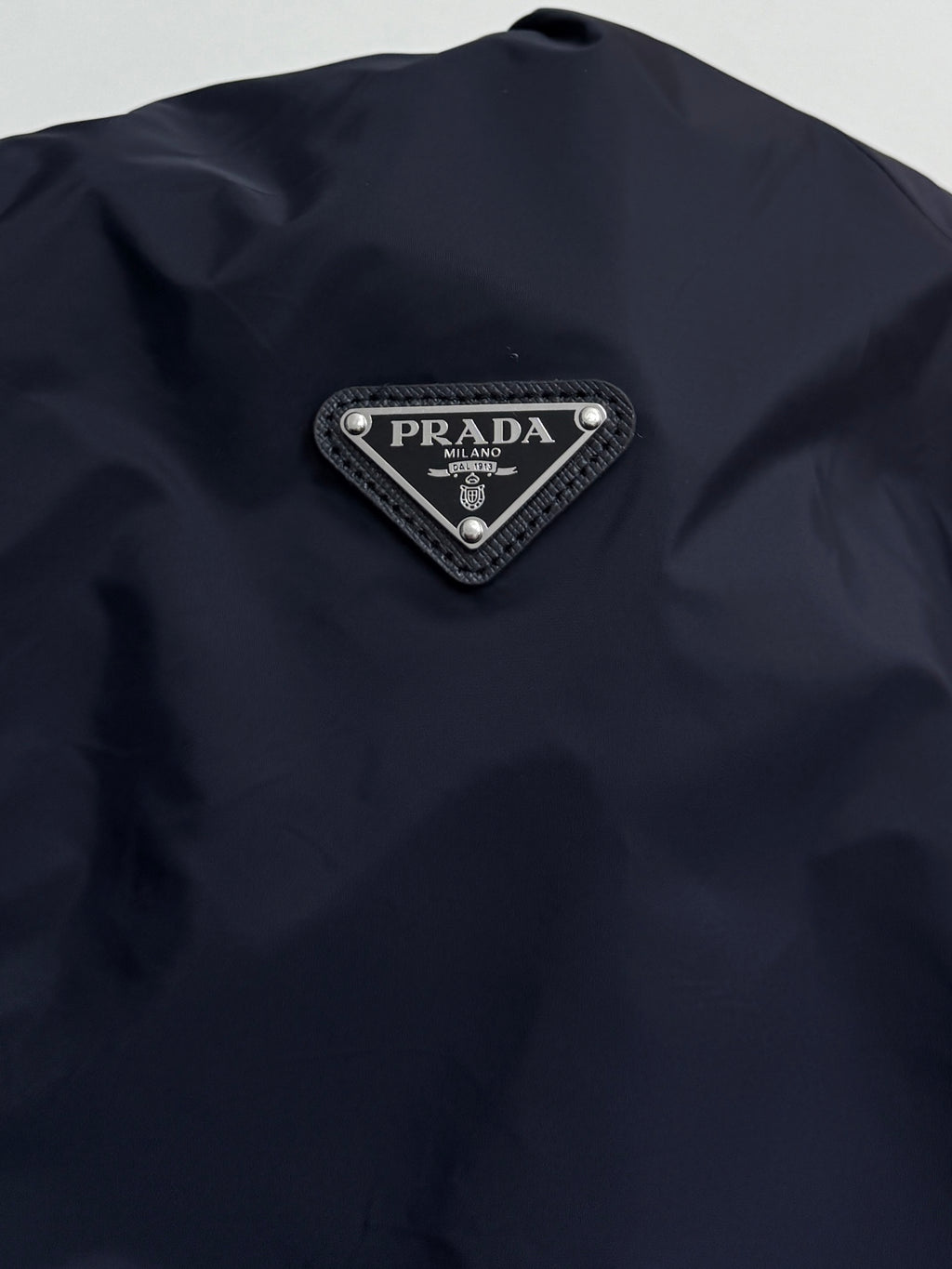 Prada triangular logo patch on dark navy jacket with silver trim