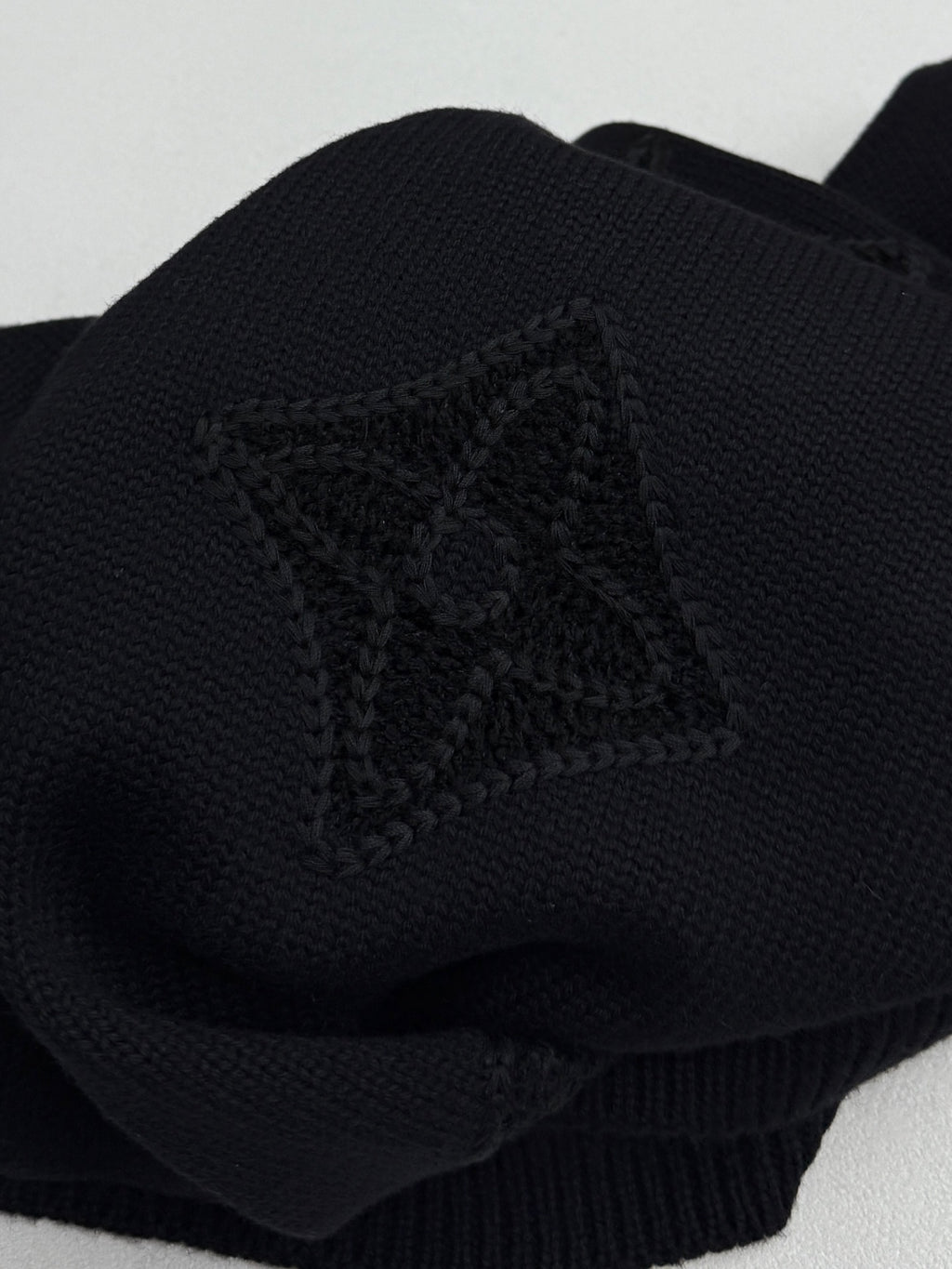Louis Vuitton sweater sleeve close-up in dark knit with embossed monogram emblem