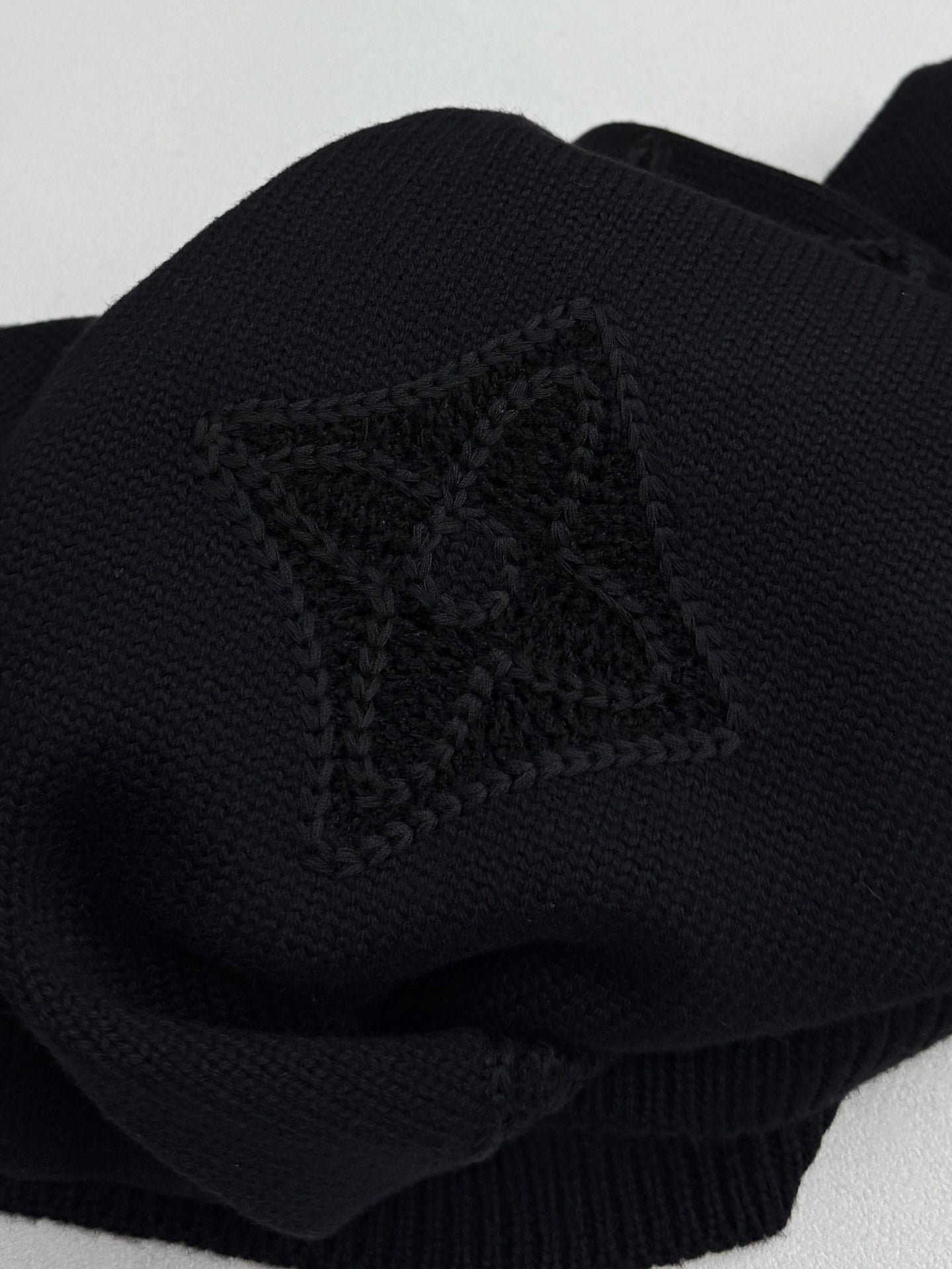 Louis Vuitton sweater sleeve close-up in dark knit with embossed monogram emblem