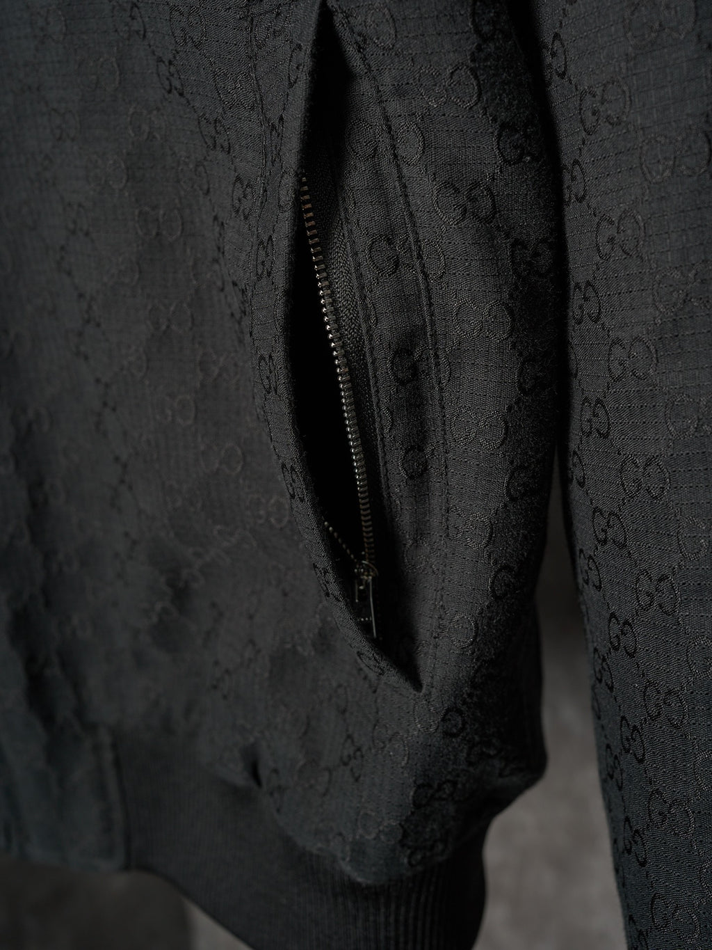 Long jacket sleeve close-up in dark allover GG pattern with diagonal zipper