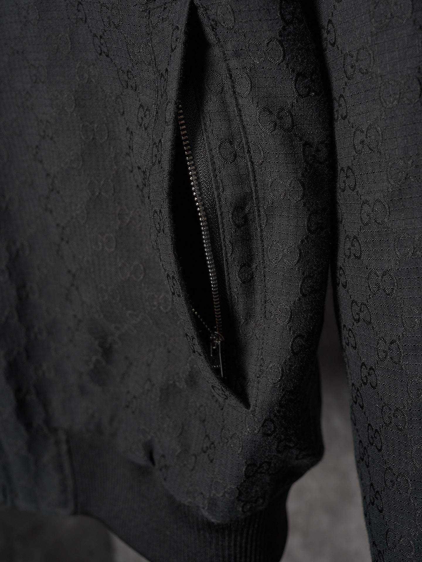 Long jacket sleeve close-up in dark allover GG pattern with diagonal zipper