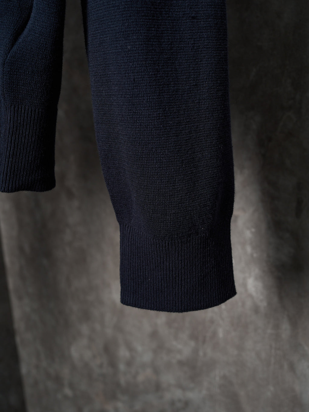 Dark navy knit sweater hem with ribbed cuffs, hanging on a hanger