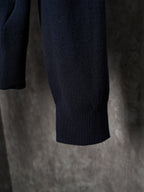 Dark navy knit sweater hem with ribbed cuffs, hanging on a hanger