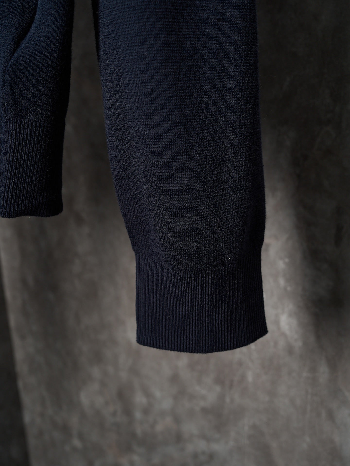 Dark navy knit sweater hem with ribbed cuffs, hanging on a hanger
