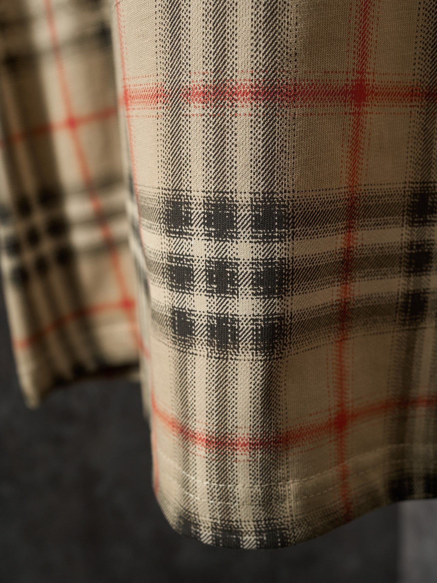Beige T-shirt fabric detail with black, red, and tan check plaid pattern