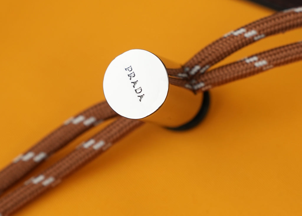 Round Prada logo label on brown braided strap end