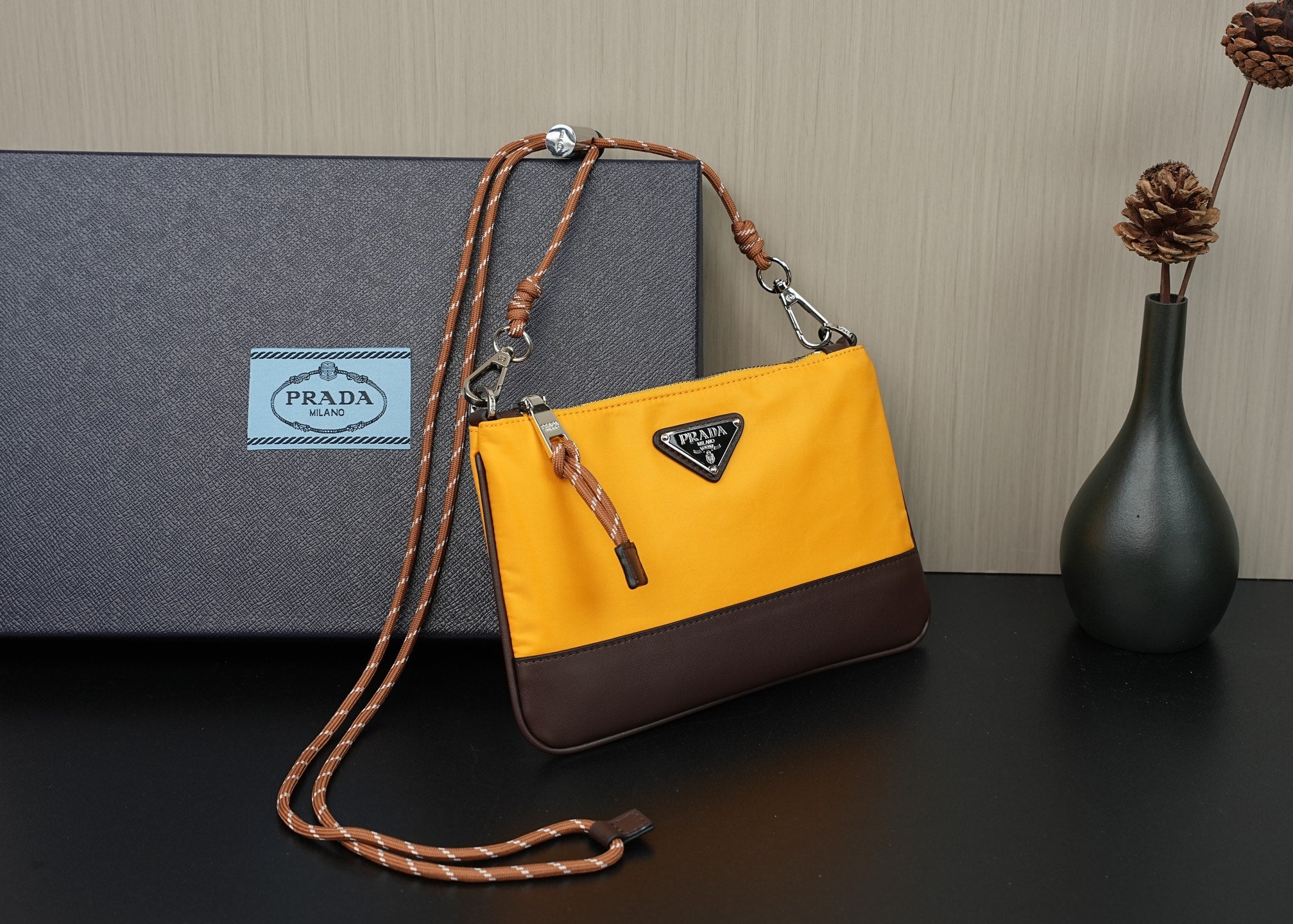Mustard yellow crossbody bag with brown flap panel, braided strap, and hanging tag