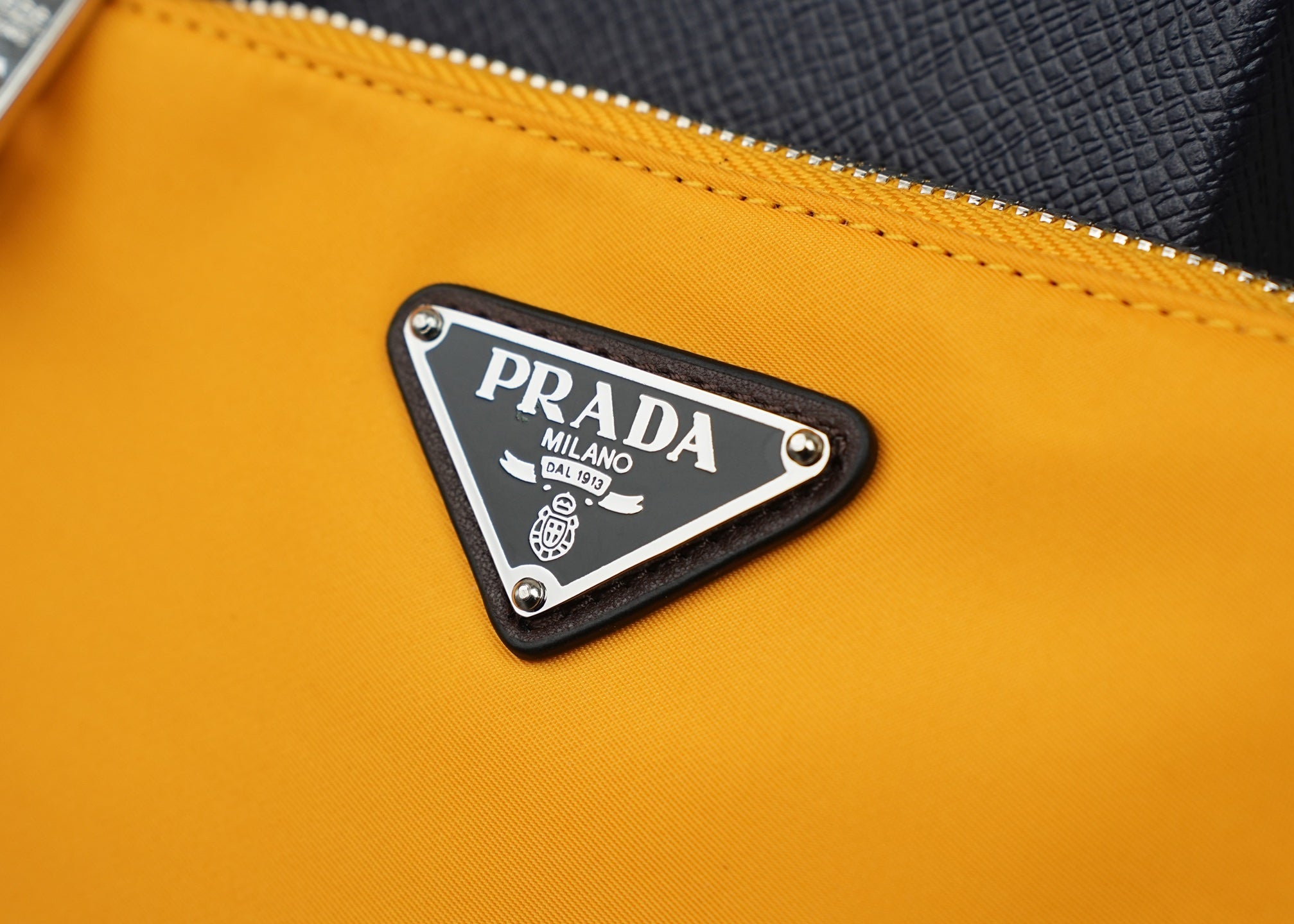 Mustard bag front with triangular Prada logo metal plaque and stitched border