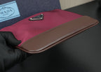 Prada handbag fold-over flap edge with dark brown trim held by gloved hand
