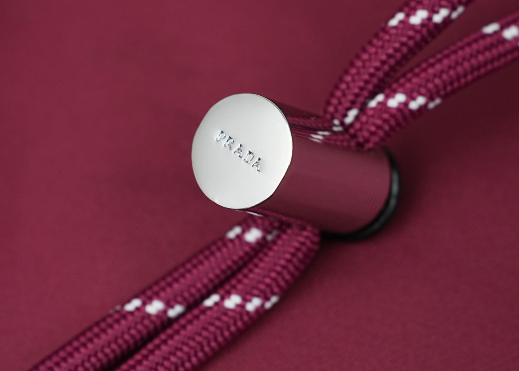 Prada handbag strap end with round metal logo tag on magenta fabric