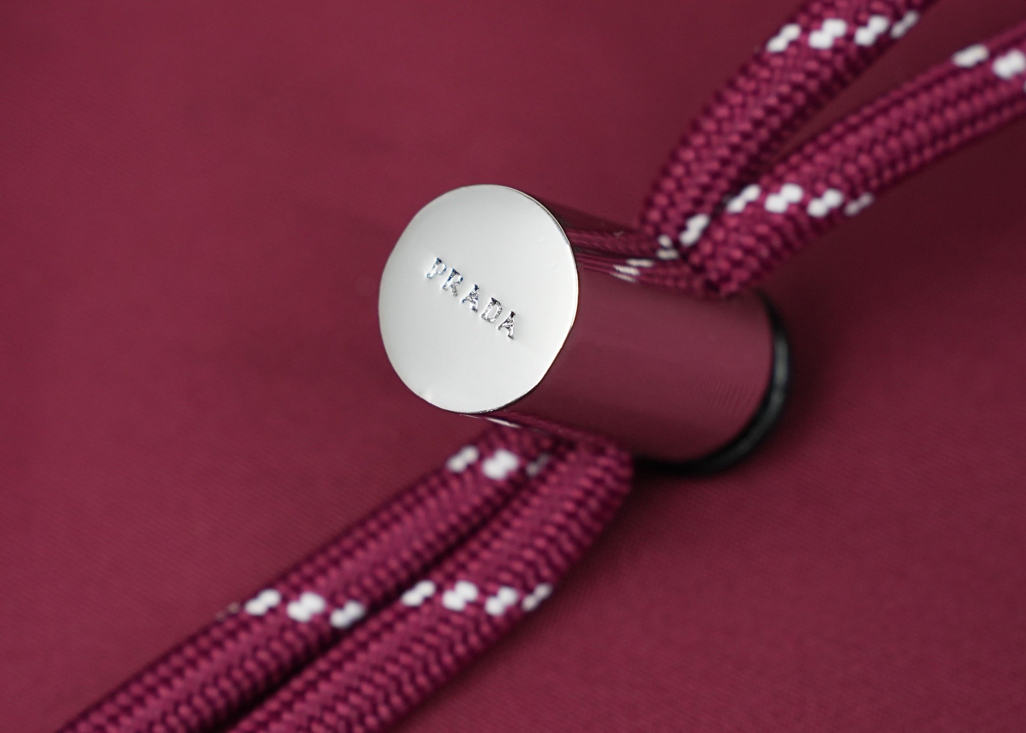 Prada handbag strap end with round metal logo tag on magenta fabric