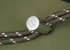 Prada bag with round metal tag on braided chain strap, lying on olive fabric
