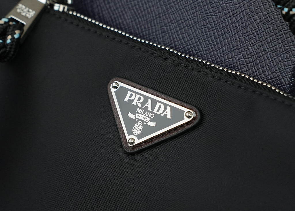 Prada metal logo plate on black textured bag with zipper and stitched edge