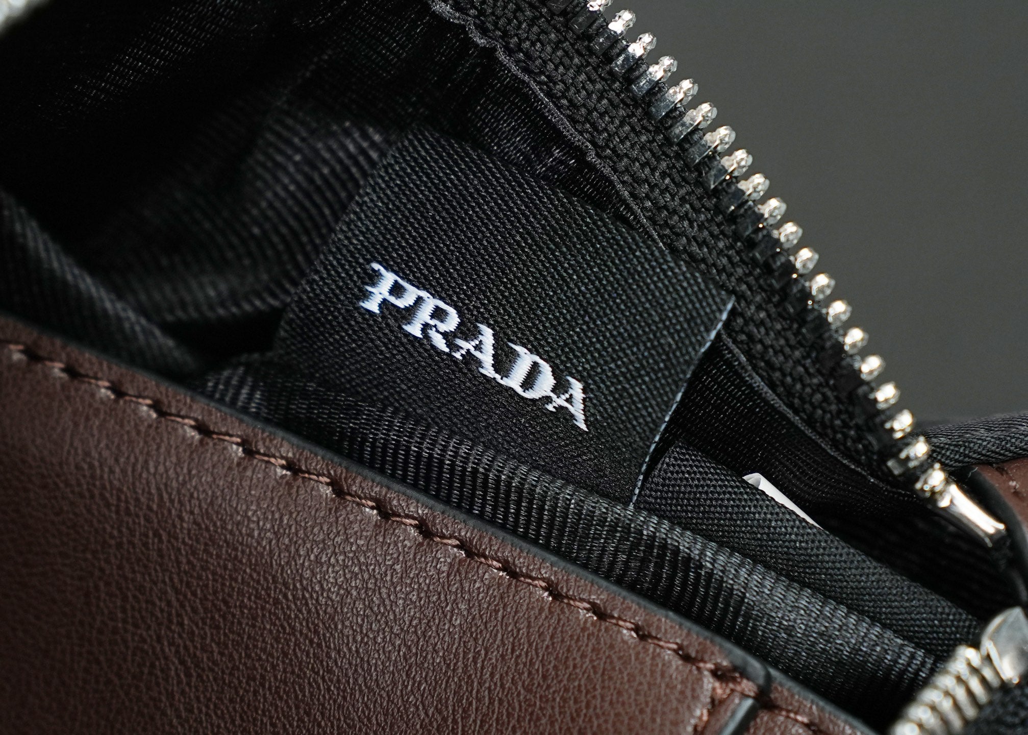 Prada logo label inside black bag lining near zipper track and brown leather trim