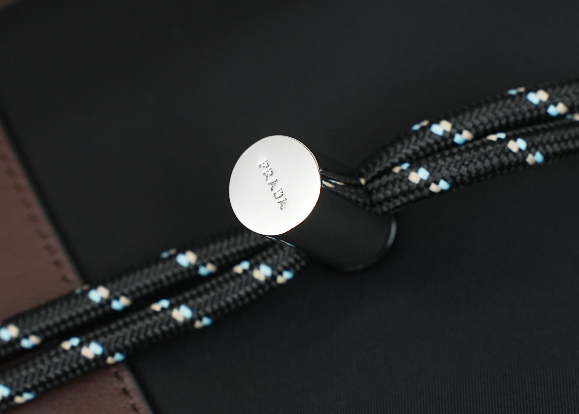 Round Prada snap button on black bag with braided beaded strap and black fabric