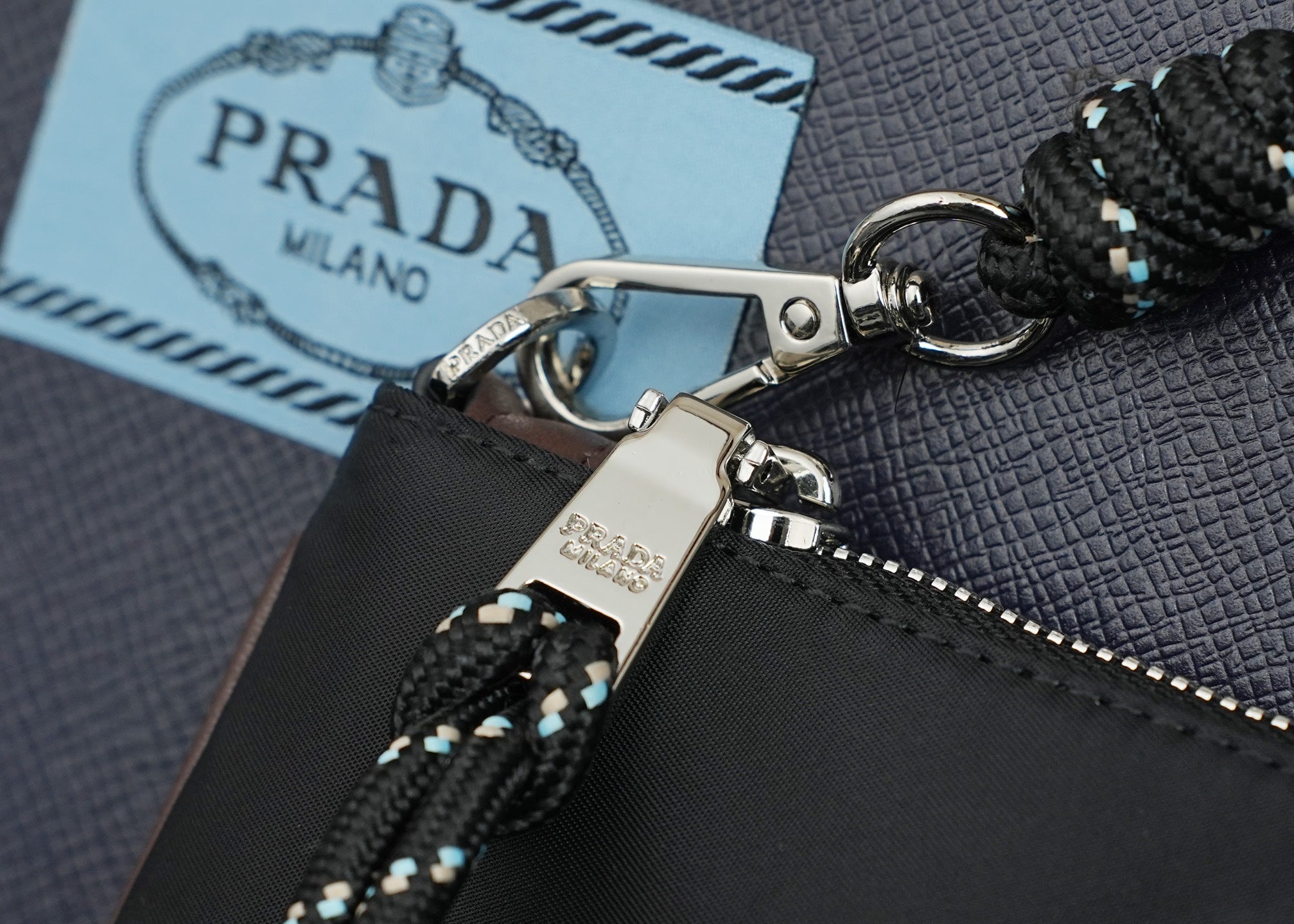 Prada strap hardware with braided black cord, silver clasp and logo tag on bag