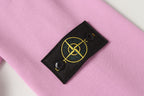 Stone Island black logo patch with yellow emblem on light pink fabric.