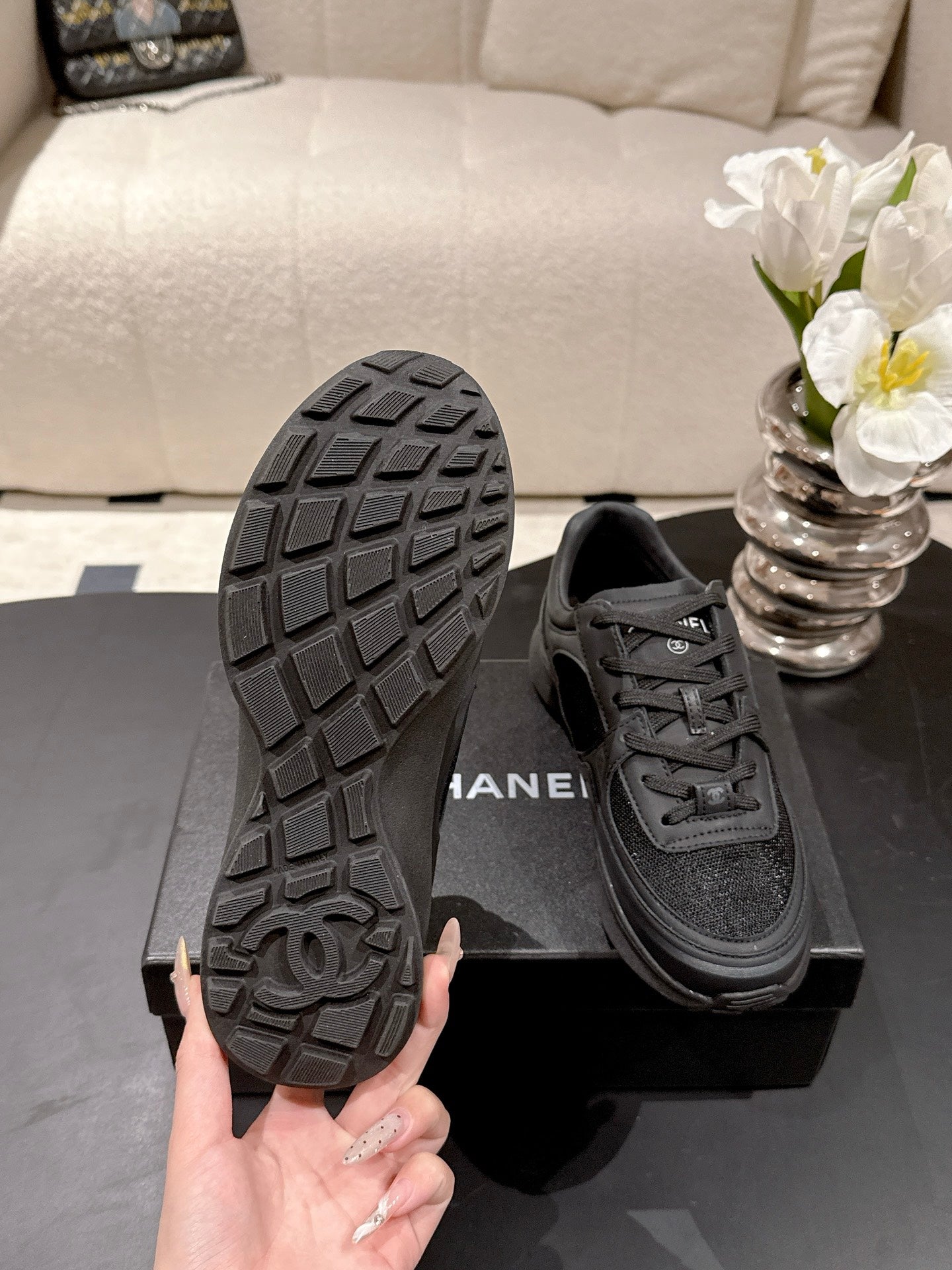 Black sneaker outsole with grid tread and Chanel logo, lace-up shoe on box