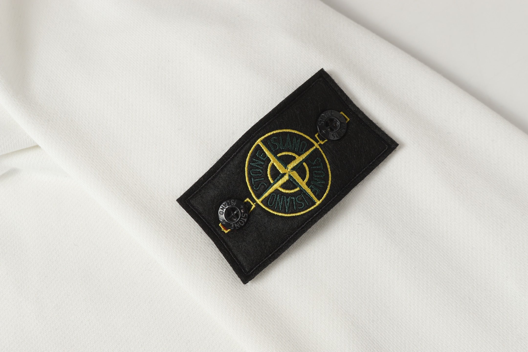Stone Island sleeve logo patch on white sweatshirt with yellow emblem detail