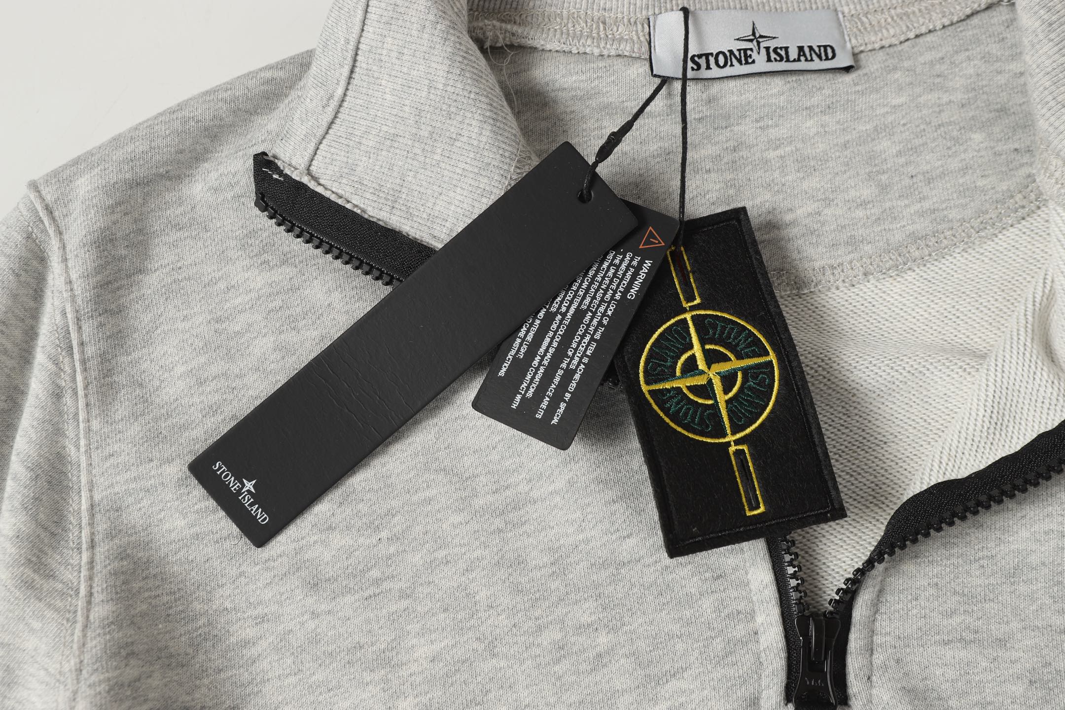 Light gray zip sweatshirt collar with Stone Island label and hanging tags