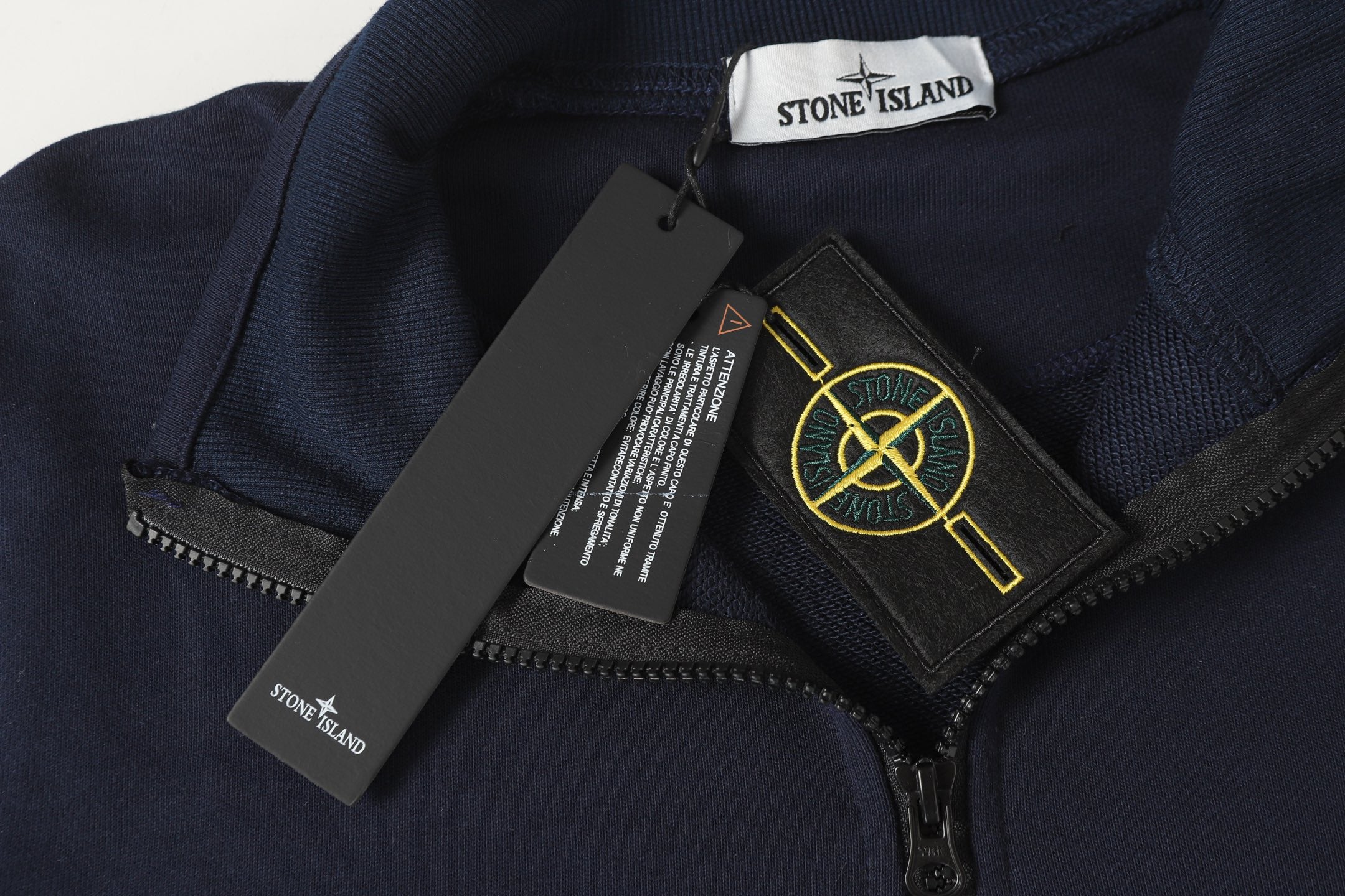 Quarter-zip sweatshirt neck area with Stone Island patch and hanging product tags.