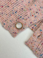 Pink speckled knit cardigan sweater detail with pearl-like button and ribbed knit placket