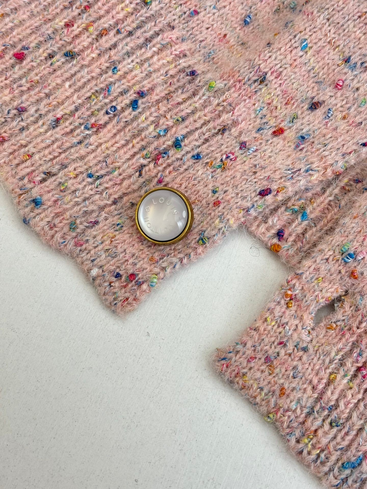 Pink speckled knit cardigan sweater detail with pearl-like button and ribbed knit placket