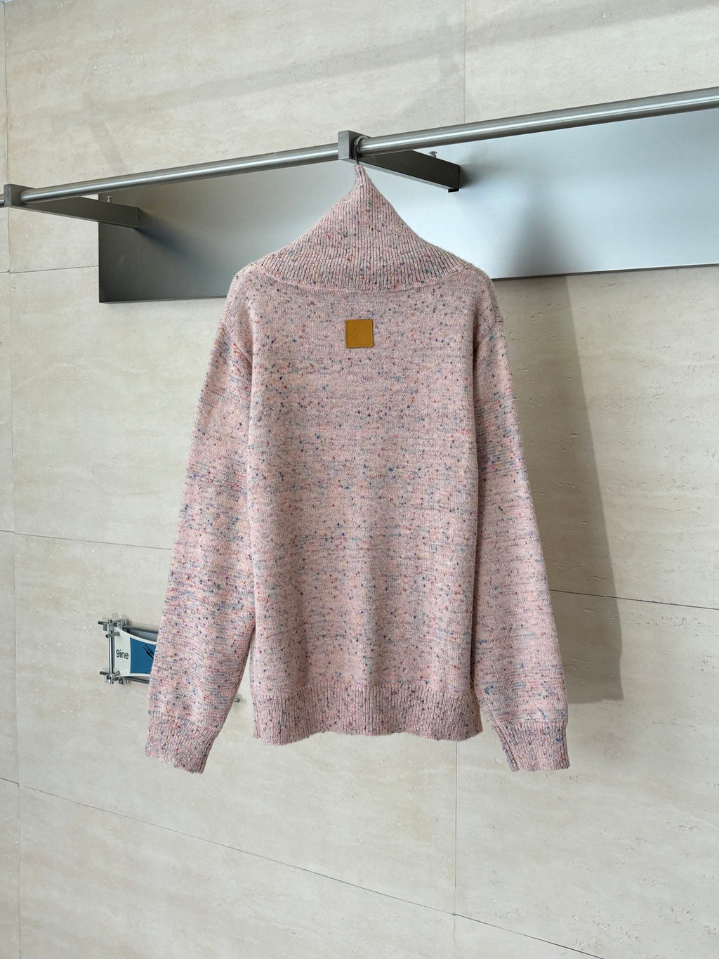 Pink speckled knit cardigan sweater on hanger, with small square logo patch on back