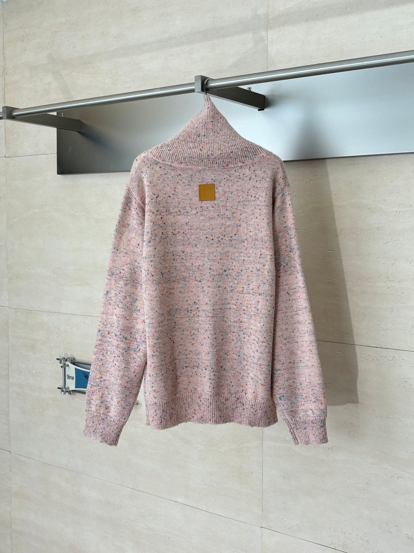 Pink speckled knit cardigan sweater on hanger, with small square logo patch on back