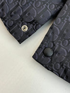 Cuff area of dark Dior monogram vest with round snap button and textured fabric.