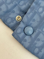 Close-up of light blue monogram vest with gold snap button and gray Dior-style logo