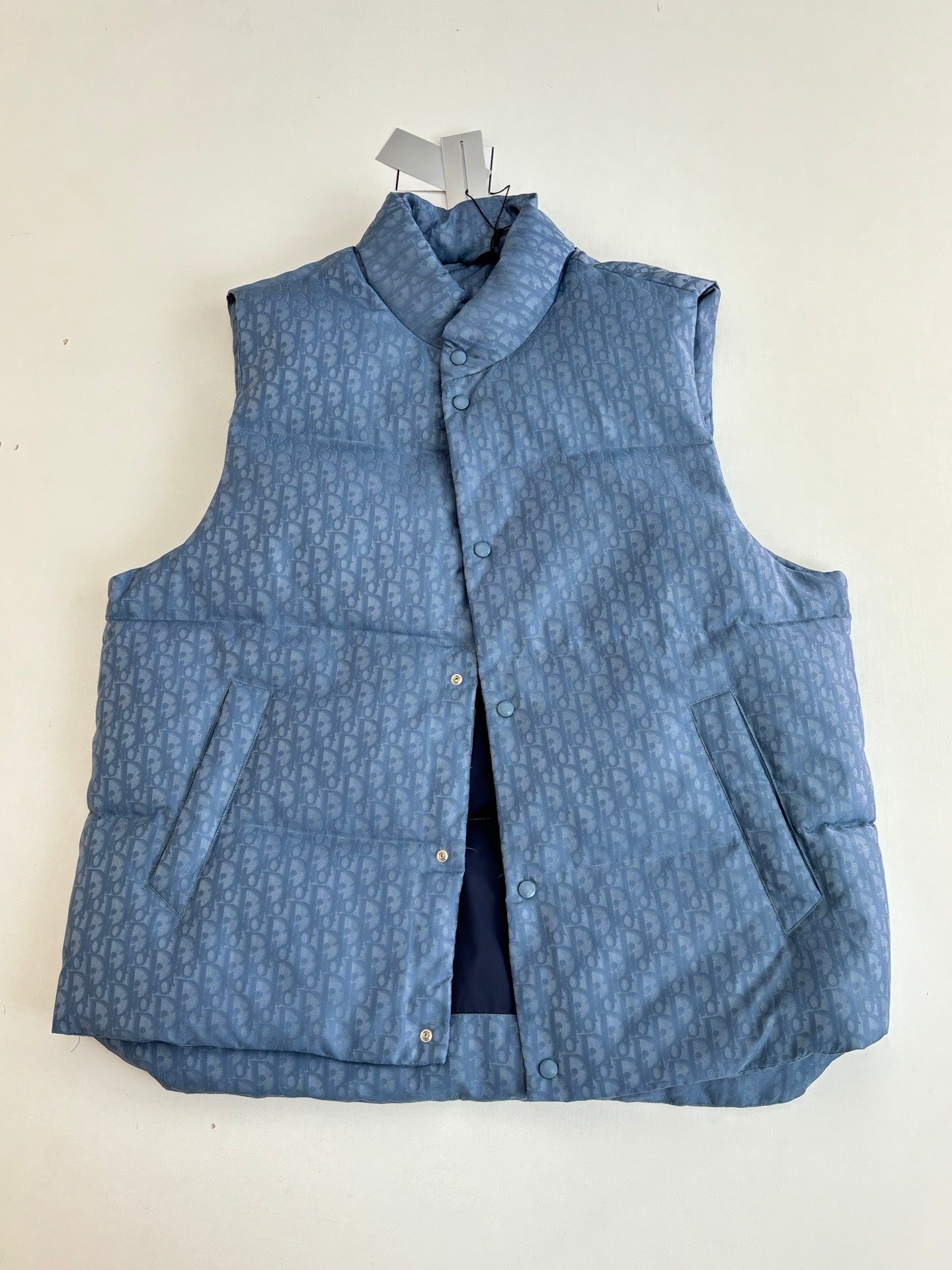 Blue sleeveless padded vest with stand collar, front buttons, and chest pocket flaps