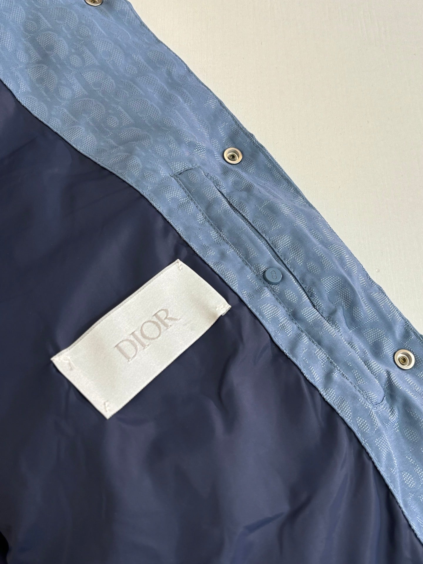 Close-up of blue sleeveless vest: dark panel, snap buttons, and Dior label tab