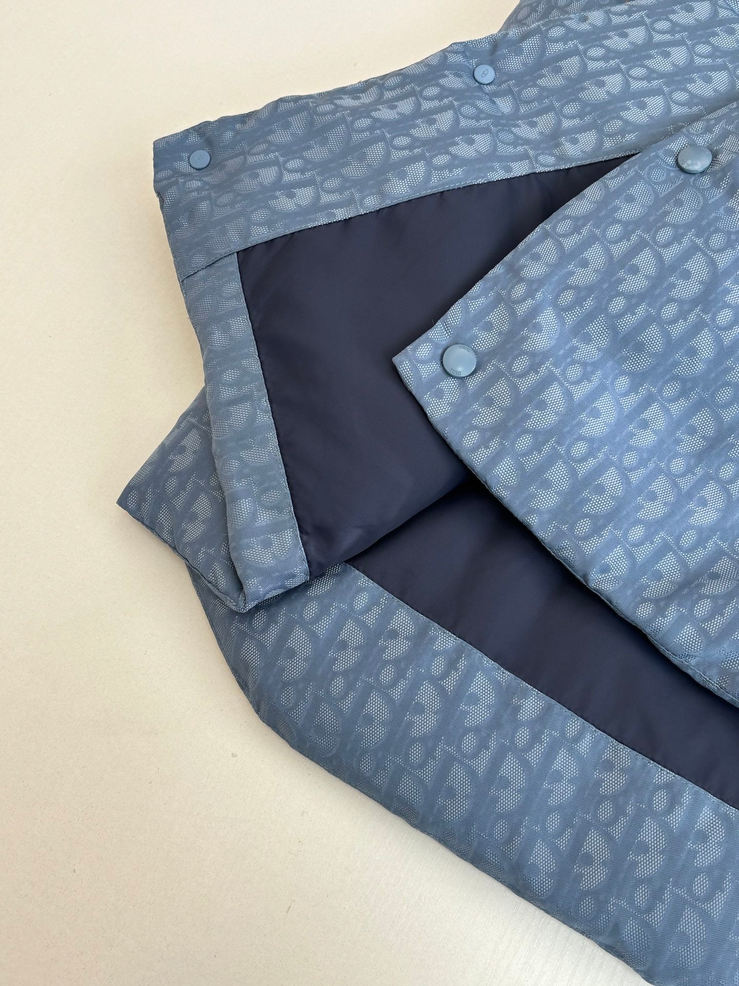 Light blue sleeveless vest with monogram pattern and dark interior panel with snap