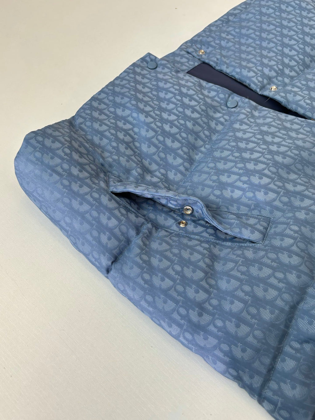 Light blue sleeveless vest with allover monogram pattern, front snaps and curved yoke