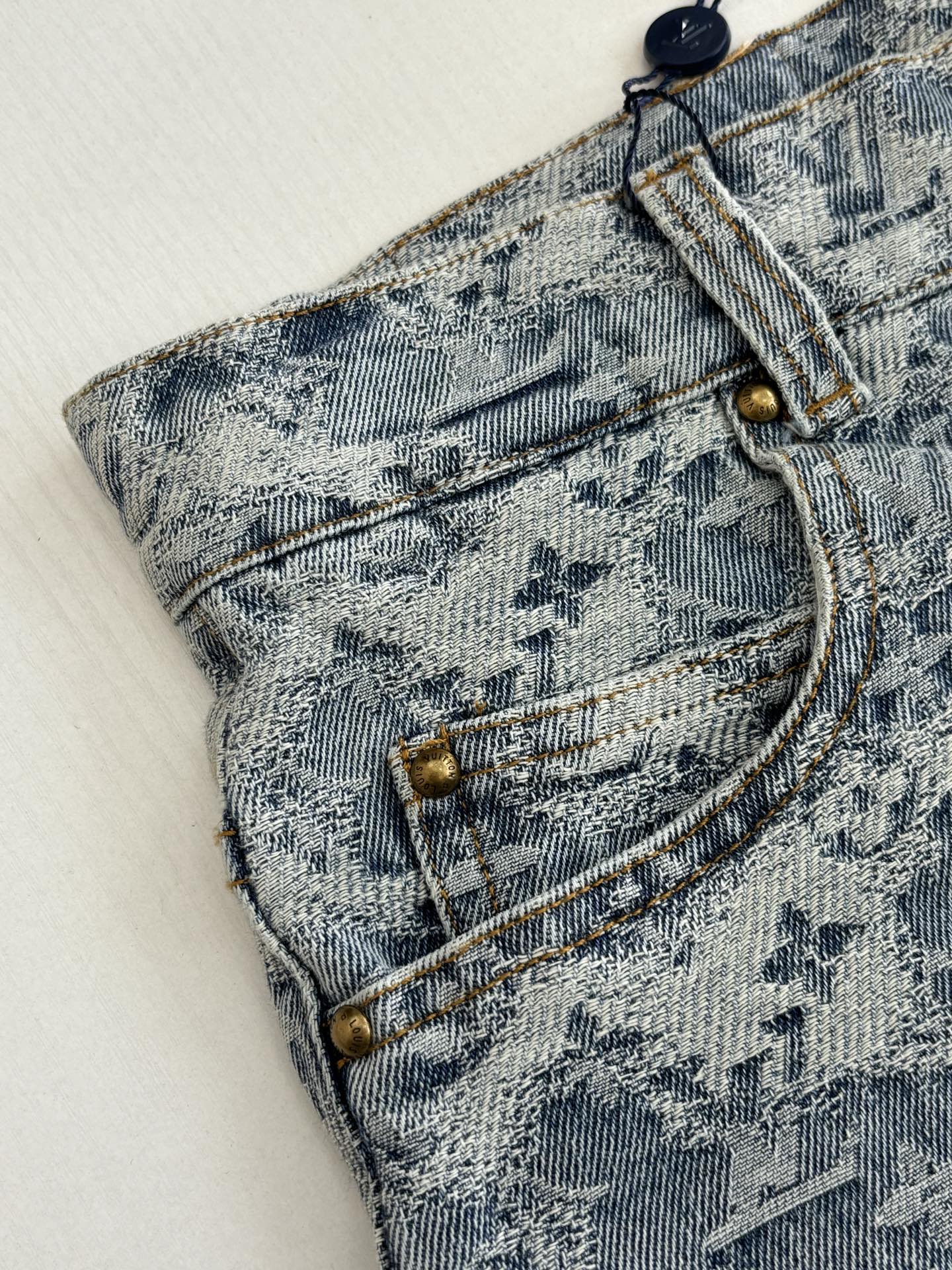 Close-up of blue monogram denim shorts: belt loops and stitched fly