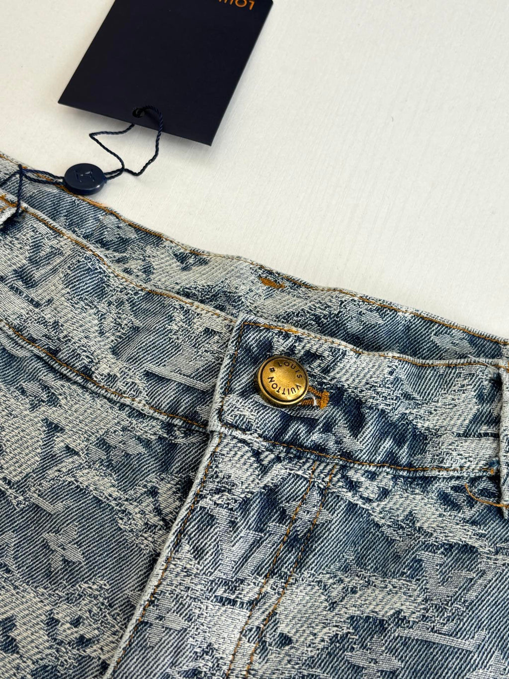 Close-up of blue monogram denim shorts waistband with gold button
