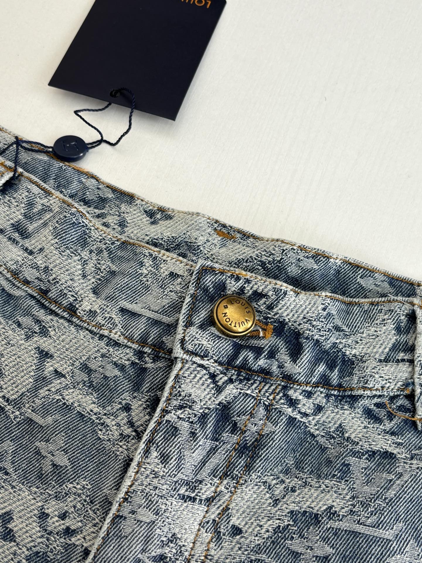 Close-up of blue monogram denim shorts waistband with gold button