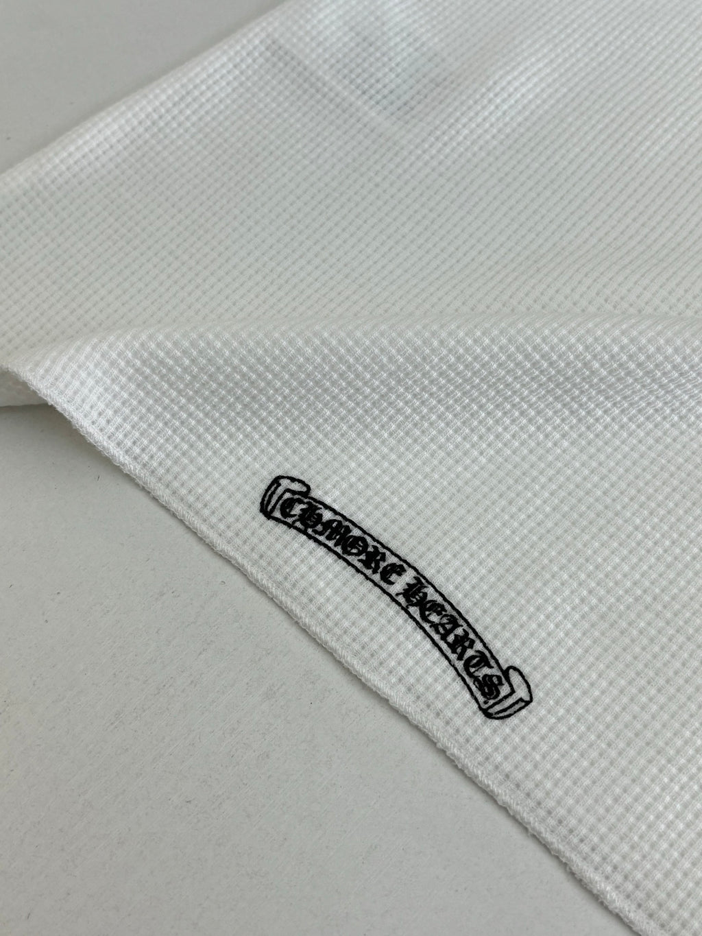 White shirt hem detail with small black logo patch