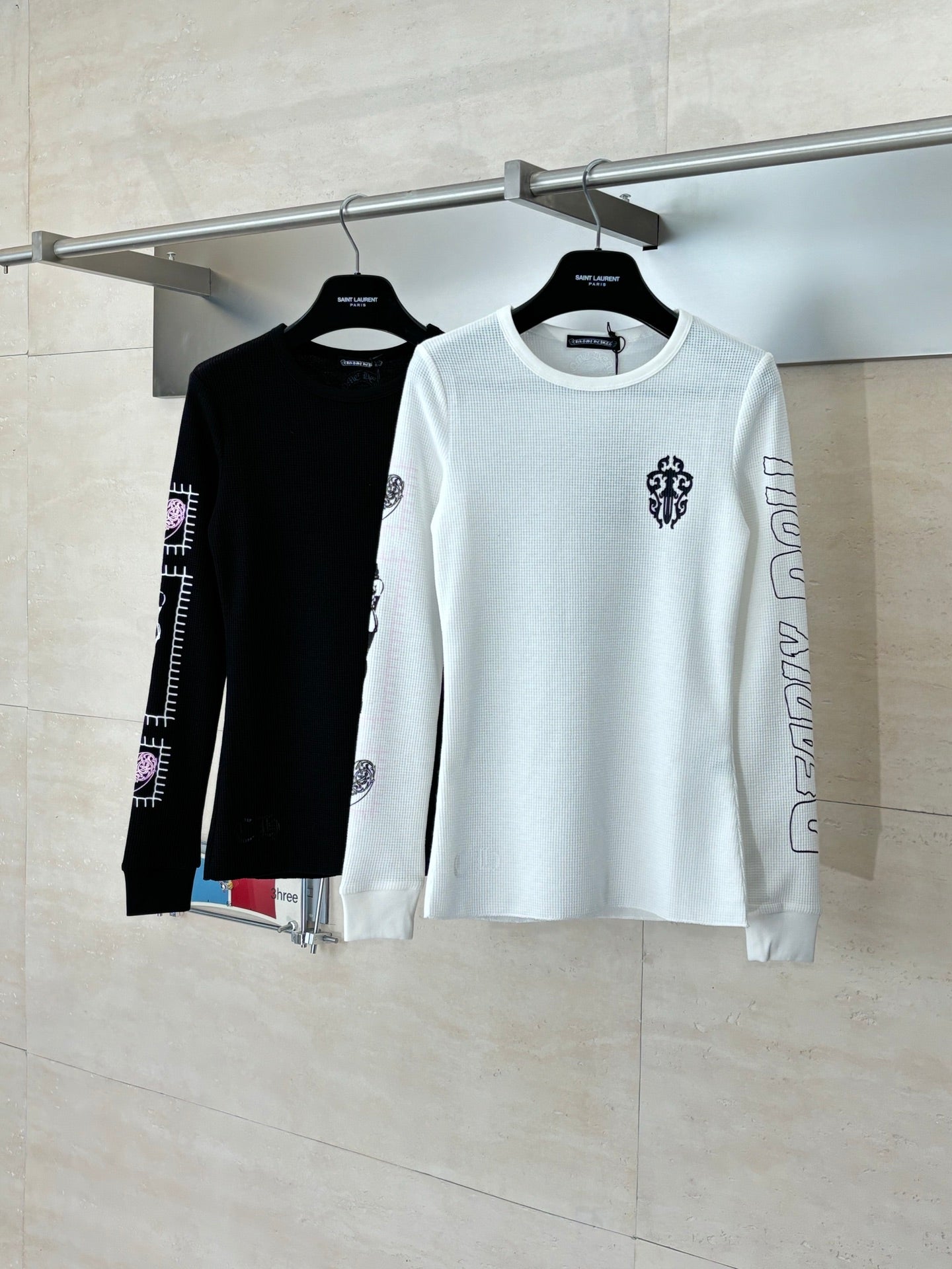 White long-sleeve crewneck shirt on hanger with sleeve and chest logo prints